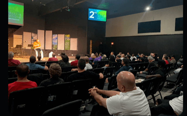 Audience seated inside a modern auditorium with a screen displaying the number 2.