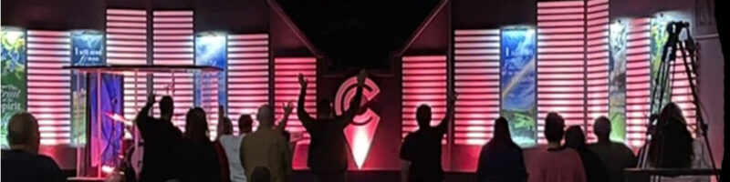 Silhouetted people raising hands in front of a stage with musical symbols and lights.